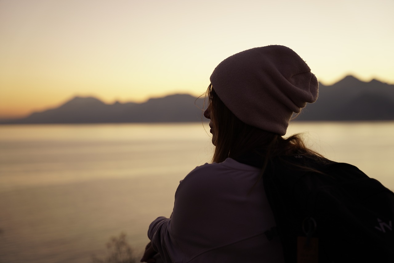Woman is sitting by the seaside in a cap. Sunset.